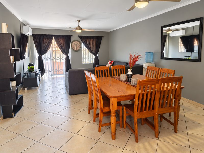 Spacious open-plan living and dining area featuring tiled flooring, ceiling fans, and air conditioning, with direct access to an outdoor patio through a security gate.