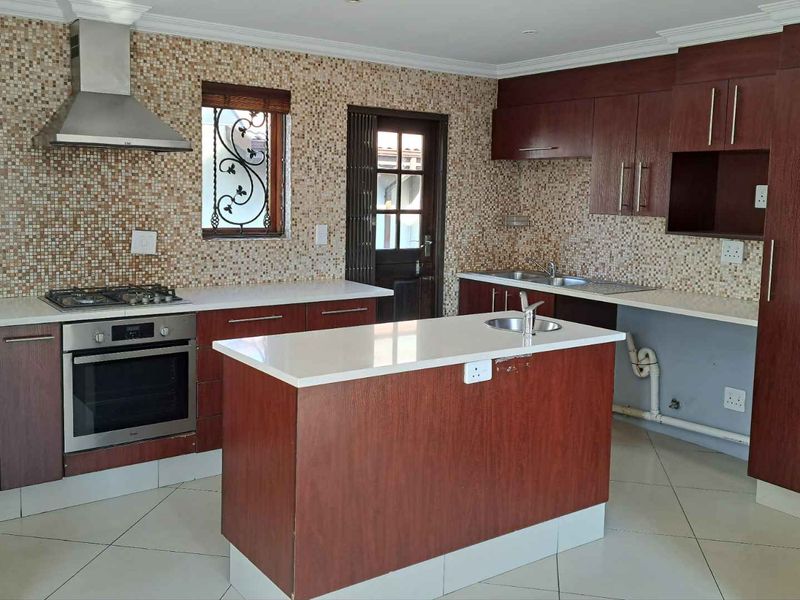 Spacious kitchen featuring dark wood cabinetry, stone countertops, a central island, and a mosaic tile backsplash, with an integrated gas hob and oven.