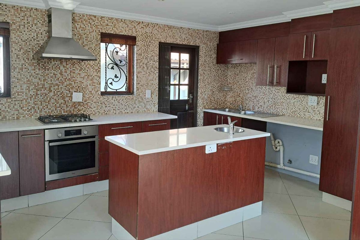 Spacious kitchen featuring dark wood cabinetry, stone countertops, a central island, and a mosaic tile backsplash, with an integrated gas hob and oven.