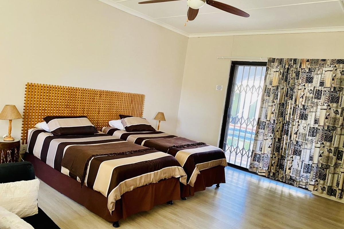 Spacious bedroom featuring light wood-look flooring, a ceiling fan, and a sliding glass door with security gate providing access to the exterior.