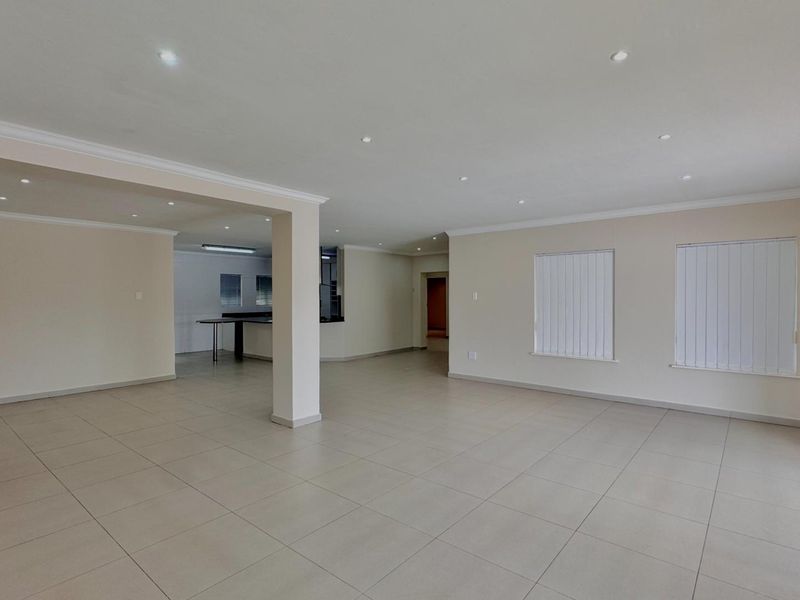 Spacious open-plan living area featuring neutral tiled flooring, recessed downlights, and direct access to the exterior through a sliding glass door.