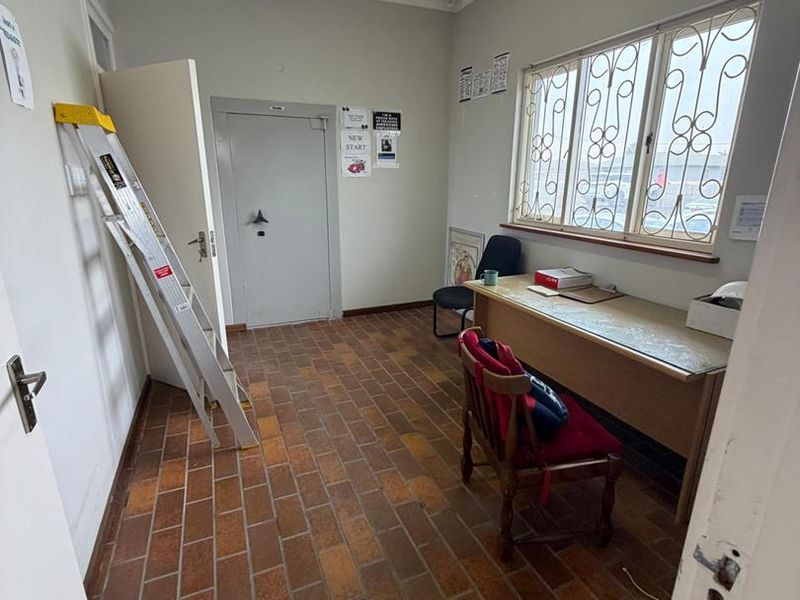 A functional office space featuring durable brick flooring, security bars on the windows, and overhead fluorescent lighting.