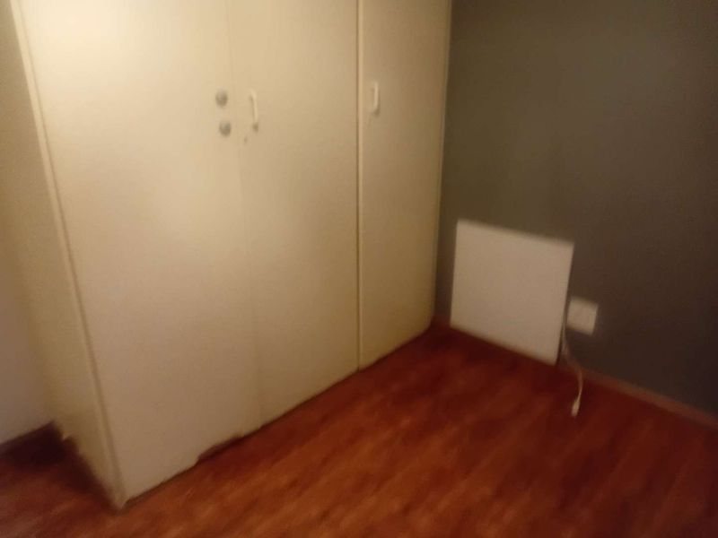 A small bedroom featuring laminate flooring and built-in cupboards with visible wear at the base.