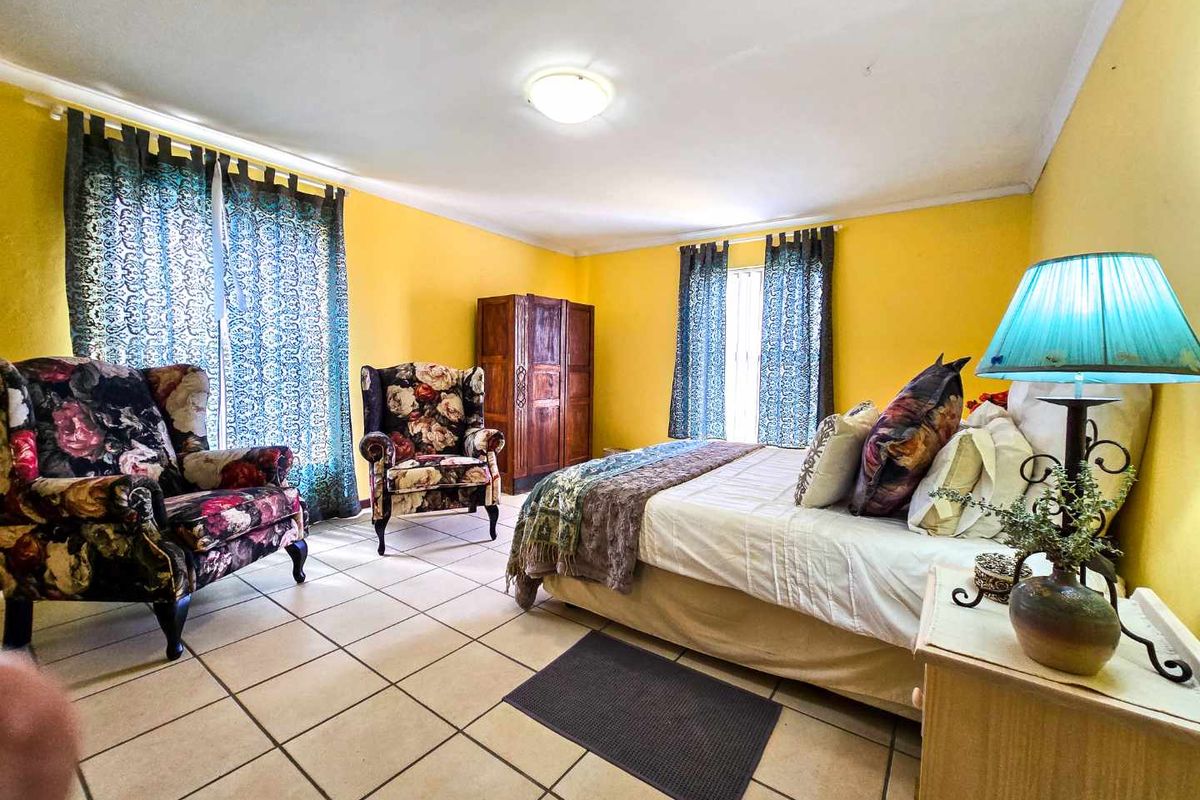 A spacious bedroom featuring tiled flooring, large windows with curtains, and a central ceiling light fixture.