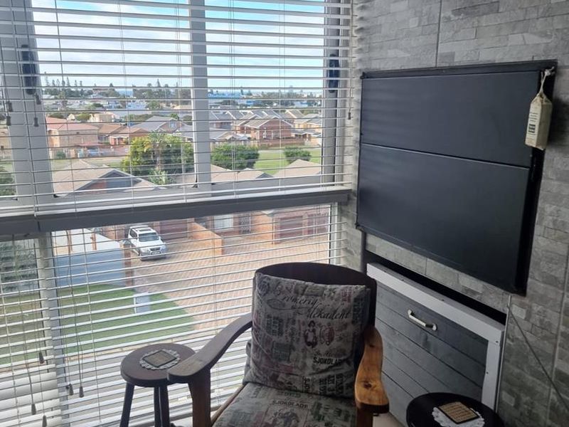 A cozy living area featuring a textured stone-cladding feature wall, large windows with venetian blinds, and neutral tiled flooring.