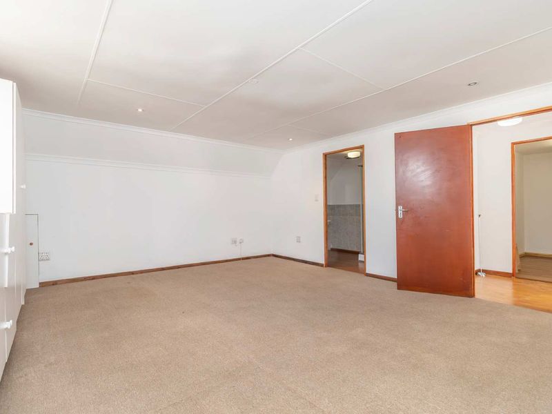 A spacious, empty bedroom featuring neutral carpeting, built-in cupboards, and direct access to an adjoining bathroom and hallway.
