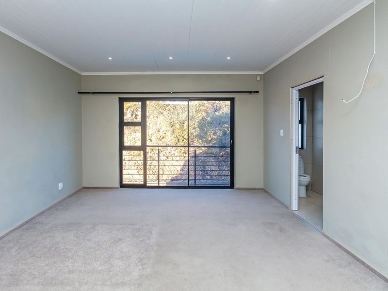 Spacious bedroom featuring neutral walls, carpeted flooring, recessed lighting, and a sliding glass door leading to an outdoor area, with an attached en-suite bathroom.