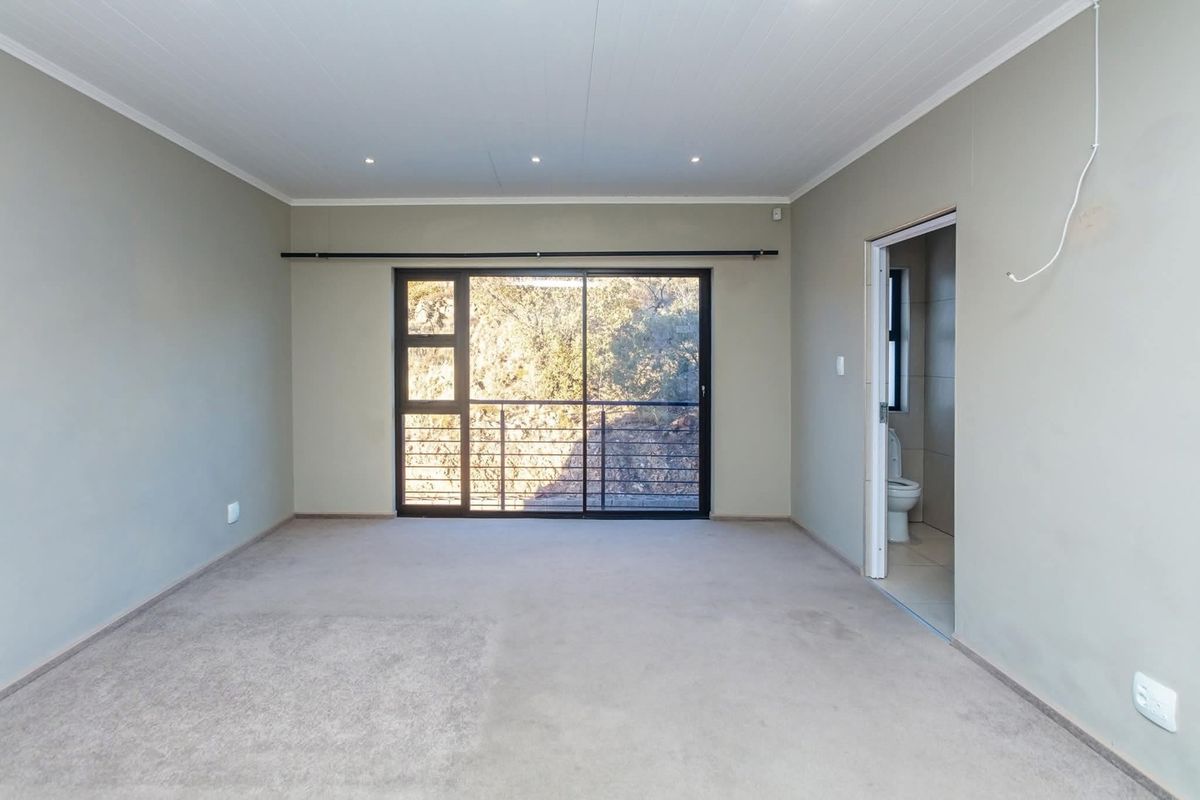 Spacious bedroom featuring neutral walls, carpeted flooring, recessed lighting, and a sliding glass door leading to an outdoor area, with an attached en-suite bathroom.