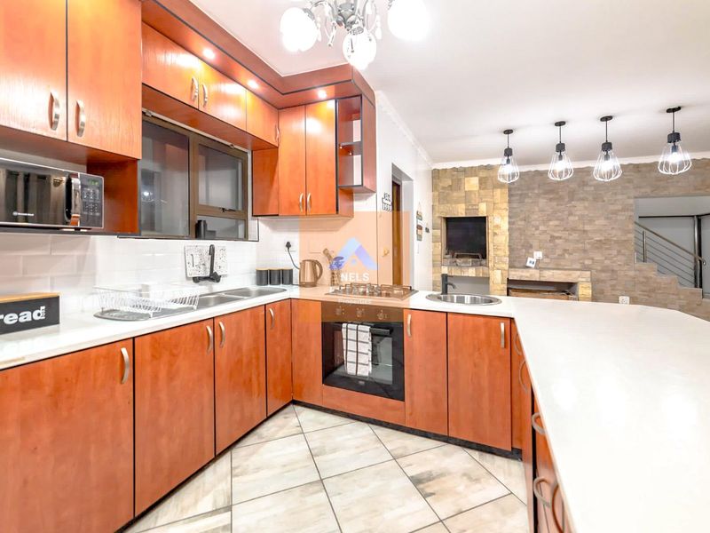 Open-plan kitchen featuring wood-finish cabinetry, stone-clad fireplace, breakfast bar, and modern built-in appliances, seamlessly connecting to the living area.