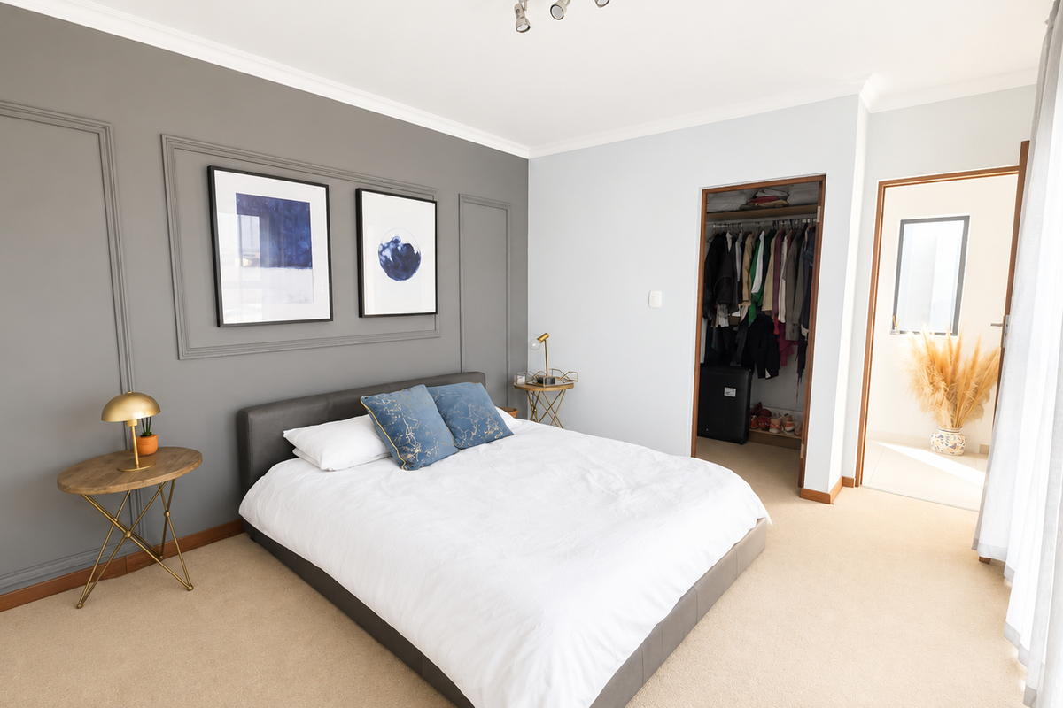 A well-maintained bedroom featuring a feature wall with decorative molding, neutral carpeting, and a convenient built-in wardrobe with access to an adjoining space.