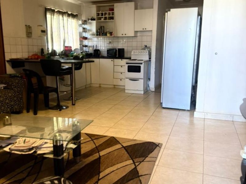 Open-plan living and kitchen area featuring tiled flooring, built-in cabinetry, and a breakfast bar, offering a functional and connected living space.