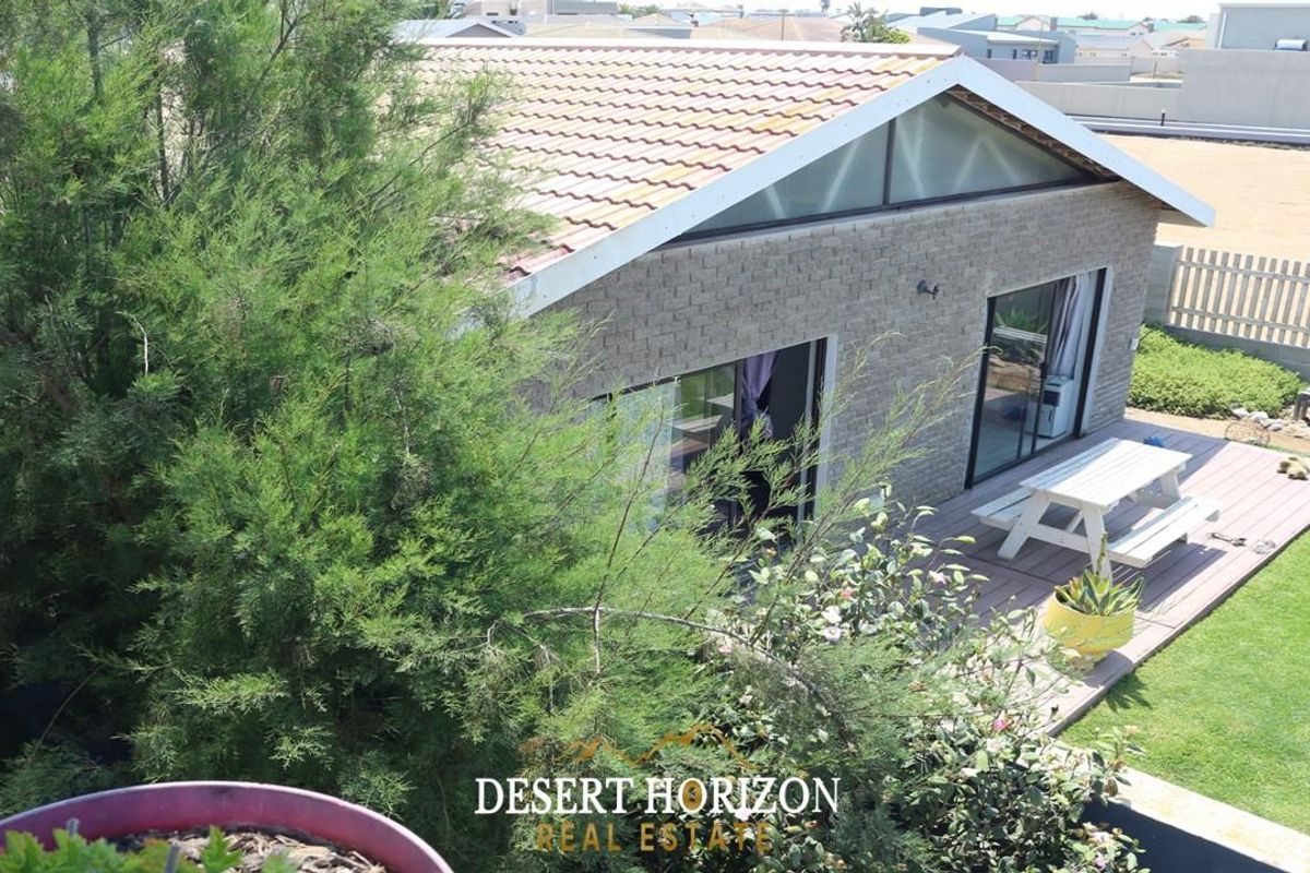 Elevated view of a rear exterior featuring a brick facade, tiled roof, timber decking, and a landscaped garden area.