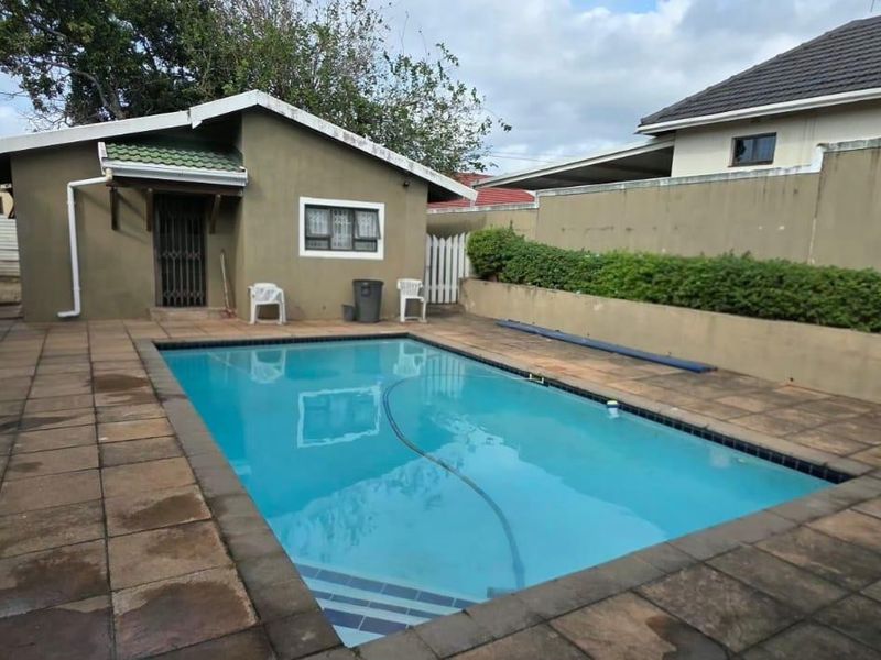 Outdoor pool area featuring a rectangular swimming pool, paved surround, and perimeter boundary wall with established hedging.