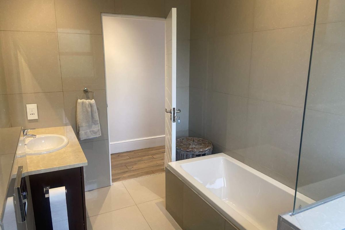 Modern bathroom featuring a built-in vanity with stone countertop, integrated basin, and a tiled bathtub with a glass shower screen.