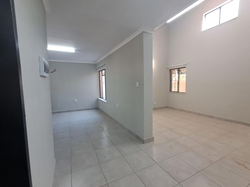 An empty, open-plan living area featuring neutral walls, tiled flooring, high ceilings with a skylight, and security bars on the windows.