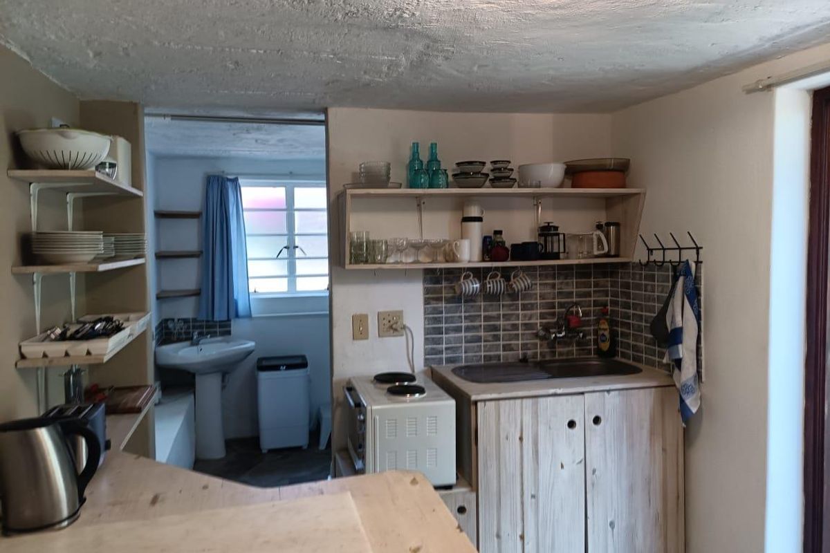A compact kitchen area featuring built-in cabinetry, a tiled backsplash, and open shelving, with an adjacent utility space visible in the background.