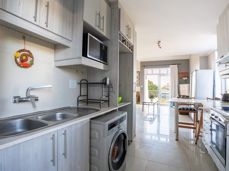 Modern open-plan kitchen and living area featuring light wood cabinetry, integrated appliances, tiled flooring, and direct access to a balcony.