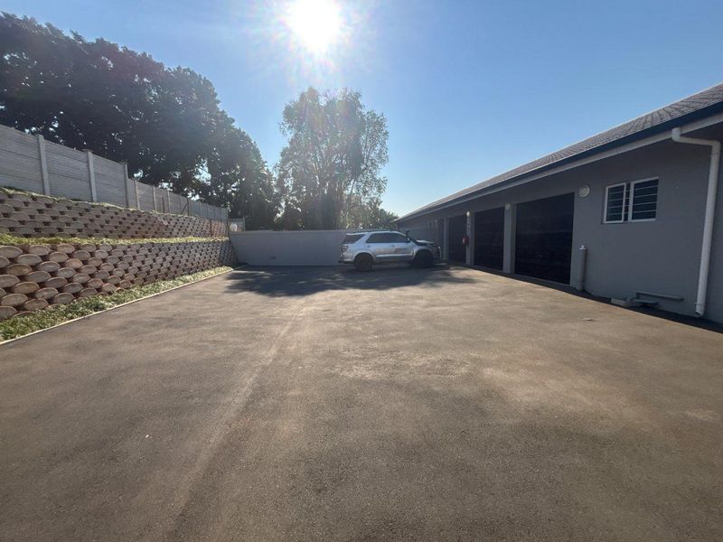 Spacious paved driveway area leading to multiple garage bays, featuring a tiered retaining wall and secure boundary fencing.