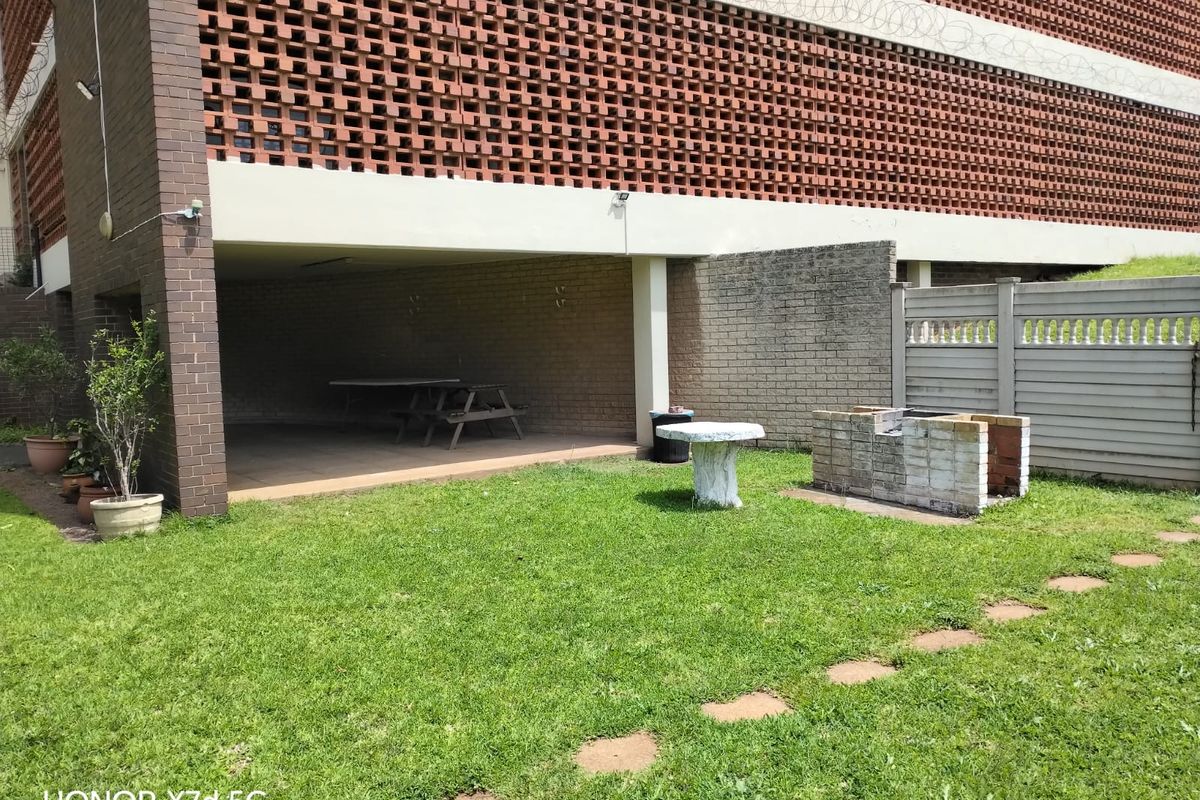 Rear exterior area featuring a covered patio, built-in brick braai, and a lawn with precast concrete boundary walling.