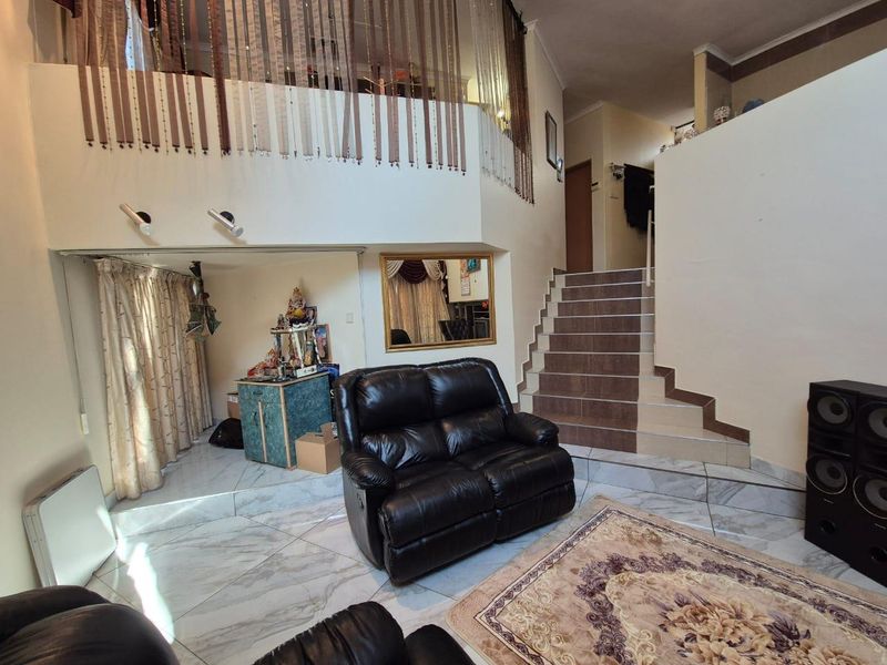 Spacious living area featuring tiled flooring, a staircase leading to a mezzanine level, and high ceilings with integrated lighting.