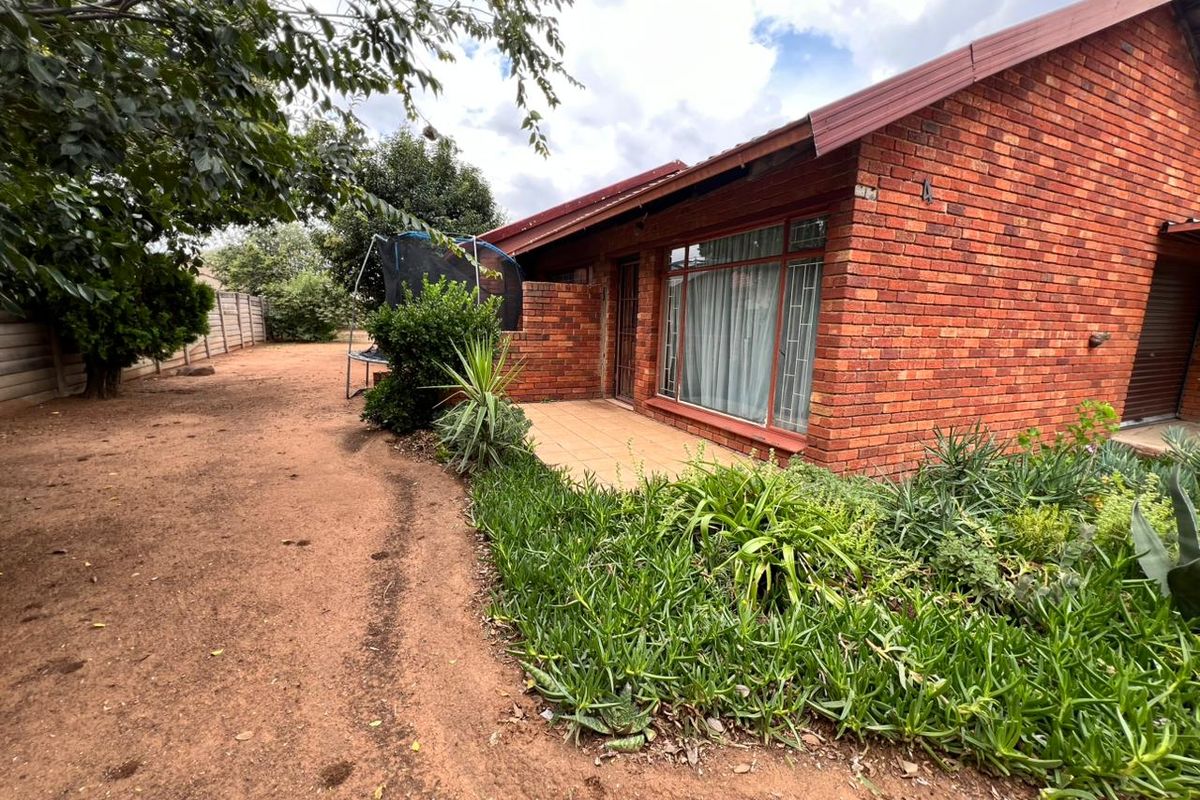 Rear view of a face brick house featuring a tiled patio area, metal window frames, and a large garden space with boundary walling.