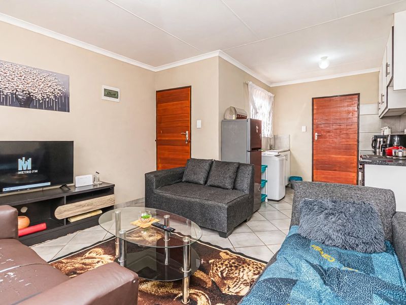 Open-plan living area featuring tiled flooring and a compact kitchen with built-in cabinetry, hob, and extractor fan.