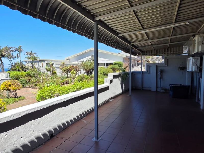 Spacious covered patio featuring tiled flooring, metal roofing, and direct access to a garden area with scenic ocean views.