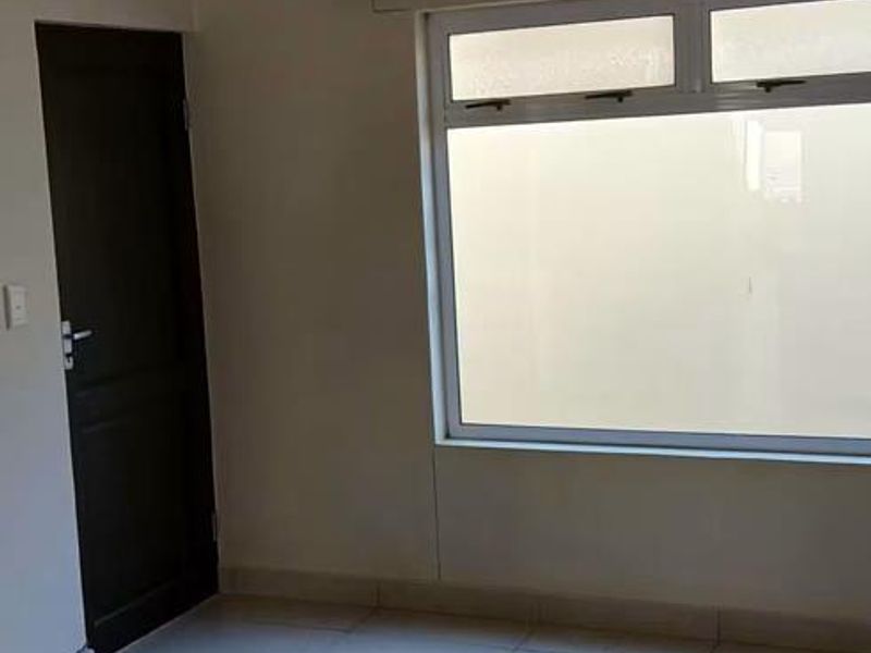 An empty bedroom featuring neutral tiled flooring, a large aluminium window, and a simple ceiling light fixture.