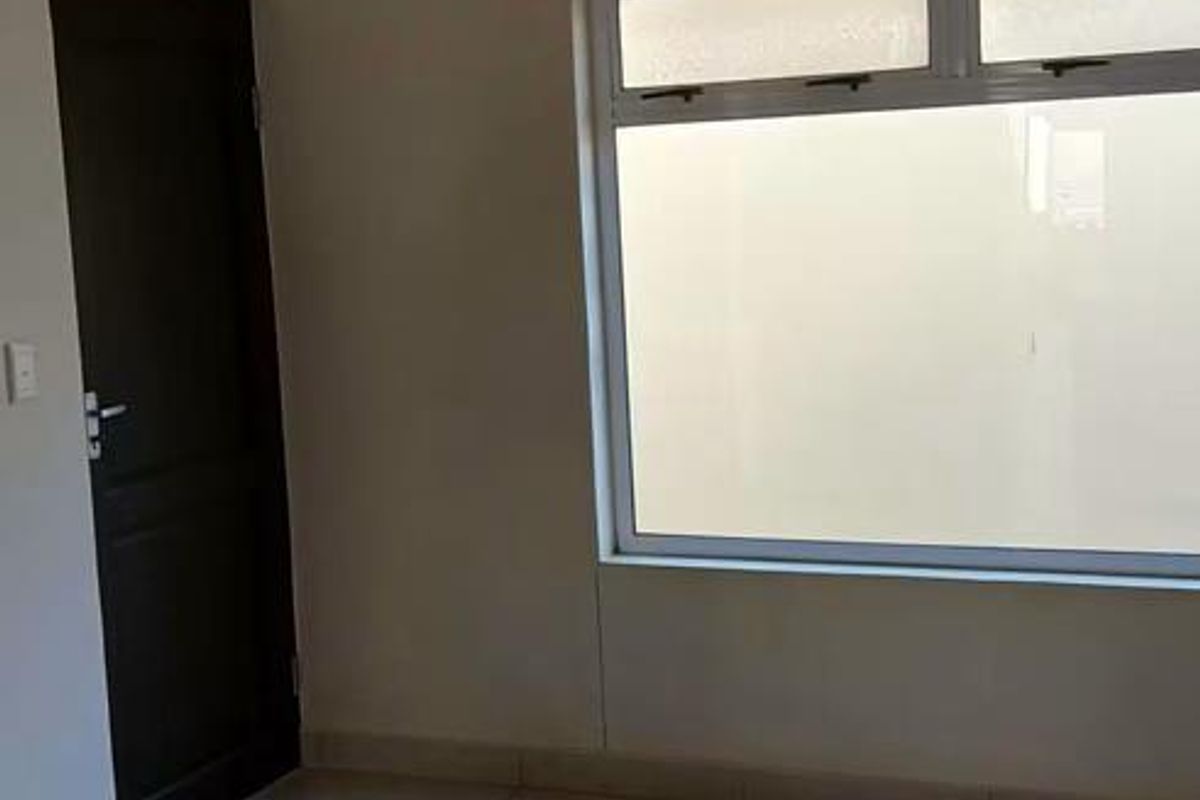 An empty bedroom featuring neutral tiled flooring, a large aluminium window, and a simple ceiling light fixture.