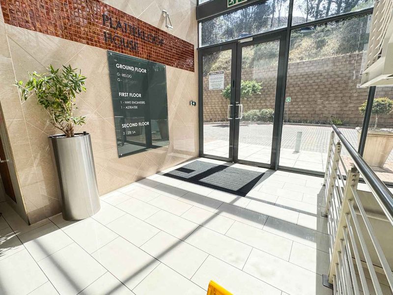 Modern commercial building entrance lobby featuring tiled flooring, glass double doors, and a clear directory signage board for tenants.