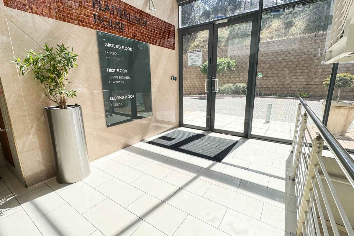 Modern commercial building entrance lobby featuring tiled flooring, glass double doors, and a clear directory signage board for tenants.
