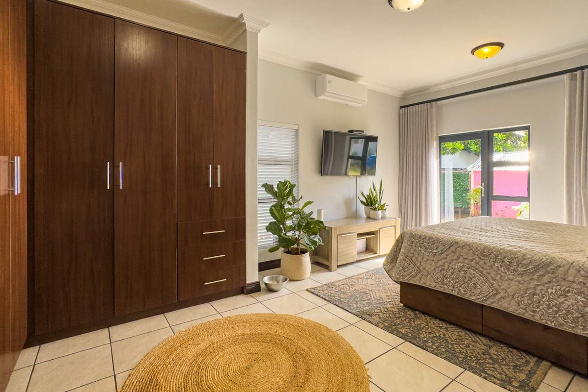 A well-lit bedroom featuring built-in dark wood cabinetry, tiled flooring, a wall-mounted air conditioning unit, and direct access to the garden through glass doors.