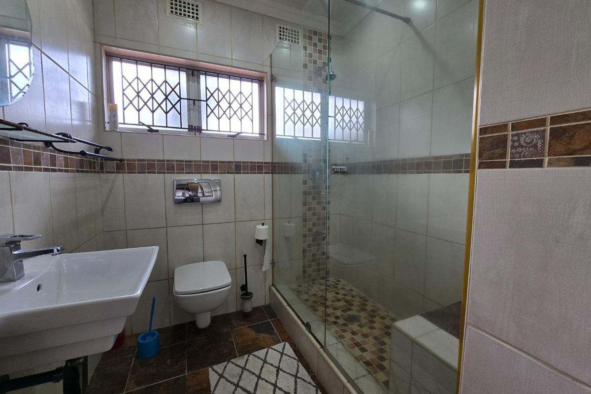 A functional bathroom featuring a wall-hung toilet, wall-mounted basin, and a glass-enclosed shower with decorative mosaic tile accents.