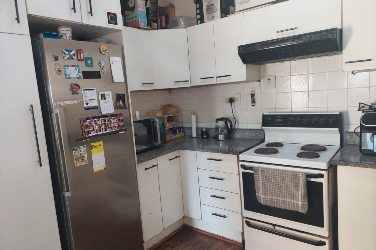 Compact kitchen featuring white cabinetry, tiled backsplash, laminate countertops, and hardwood flooring, providing a functional layout for daily meal preparation.
