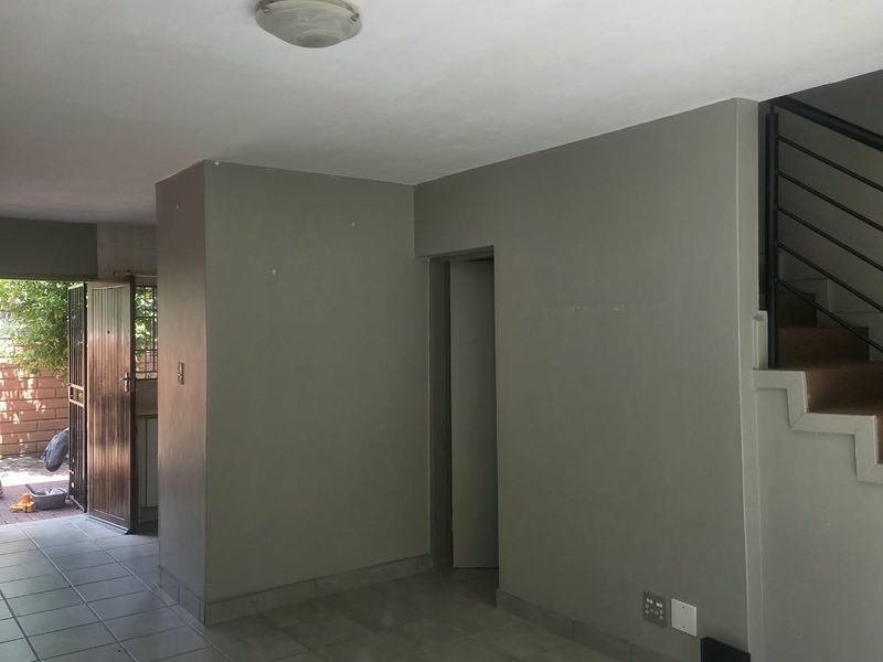 An open-plan living area featuring tiled flooring, a staircase with a metal railing, and direct access to an outdoor space through a security gate.