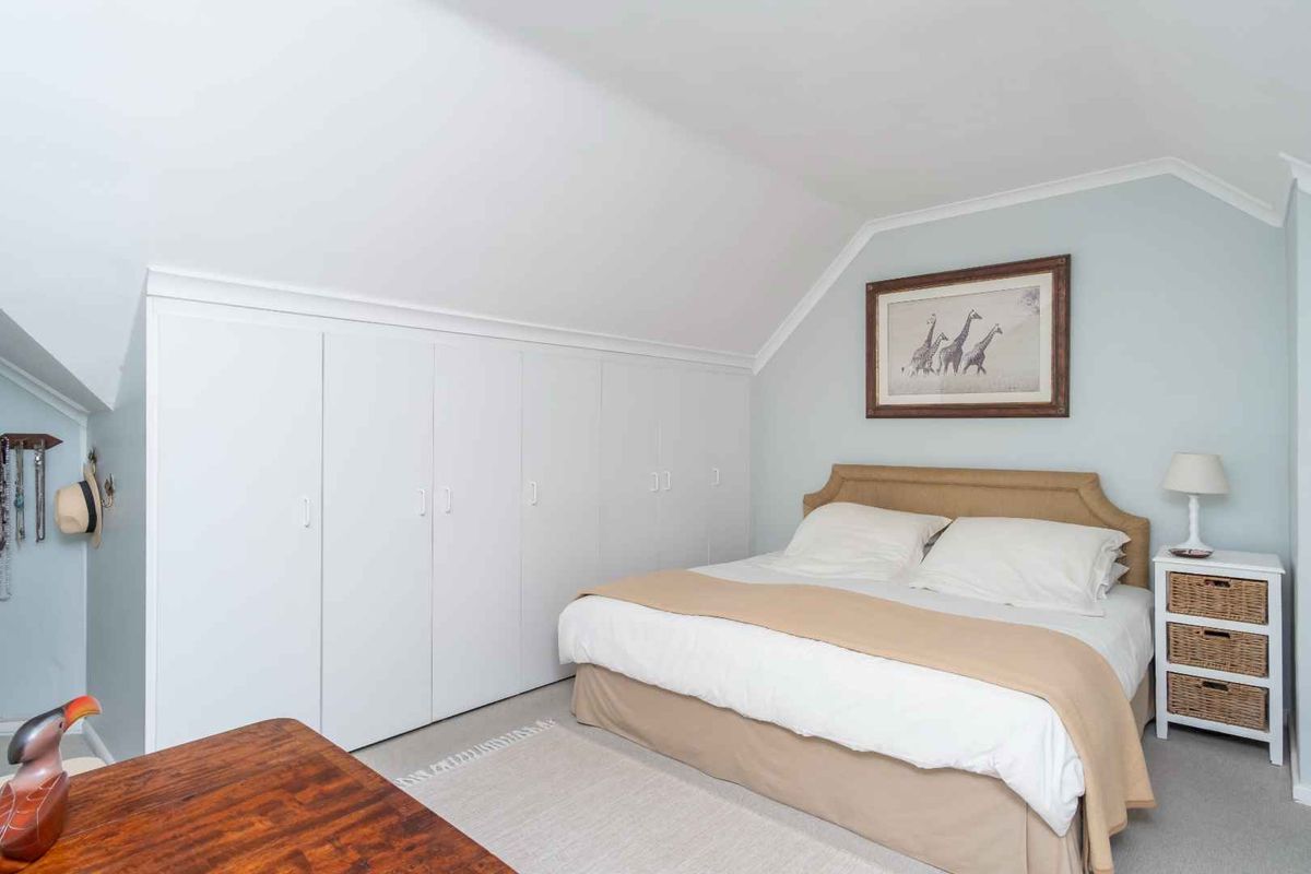 A well-maintained bedroom featuring extensive built-in cupboards, a sloped ceiling with coving, and neutral wall finishes.