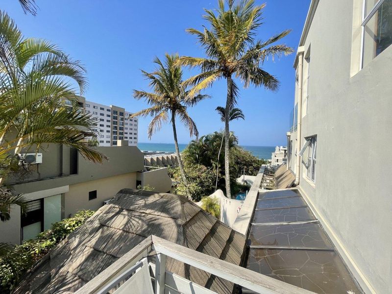 Elevated view from a townhouse balcony overlooking the surrounding estate, palm trees, and the ocean in the distance.