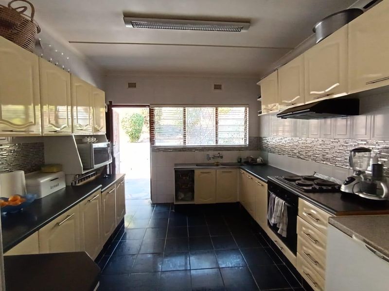 Functional kitchen featuring cream cabinetry, dark countertops, tiled backsplash, and built-in cooking appliances with direct access to the rear exterior.