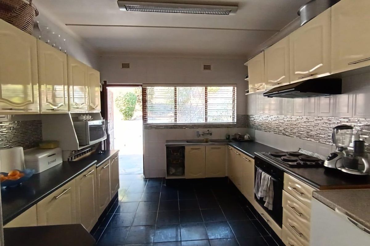 Functional kitchen featuring cream cabinetry, dark countertops, tiled backsplash, and built-in cooking appliances with direct access to the rear exterior.