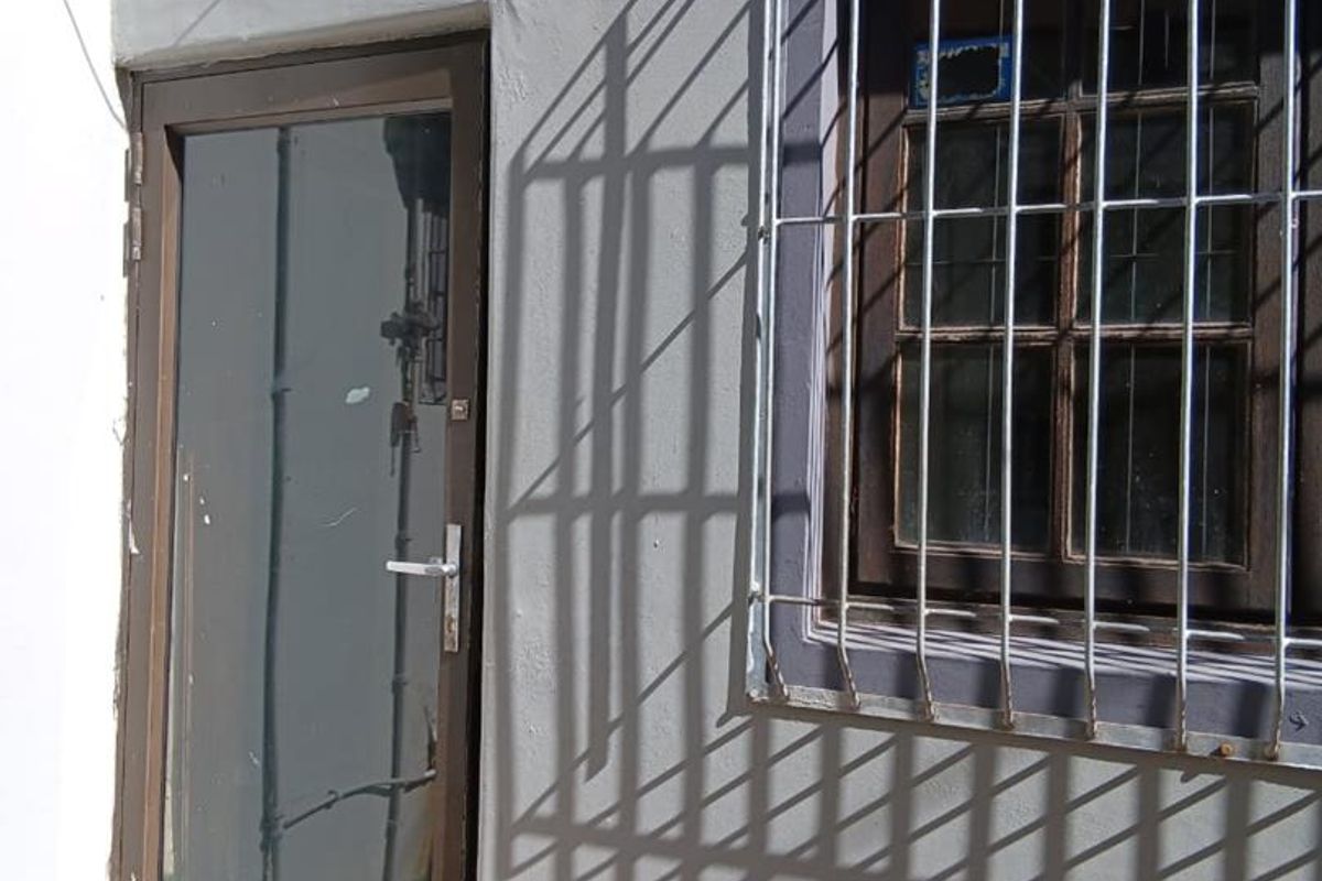 Exterior view of a building facade featuring a glass-panelled door and a window protected by security bars.