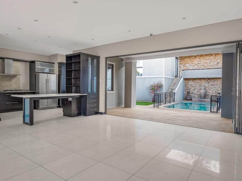 Spacious open-plan living and kitchen area featuring modern cabinetry, tiled floors, and seamless indoor-outdoor flow to a private patio and swimming pool.