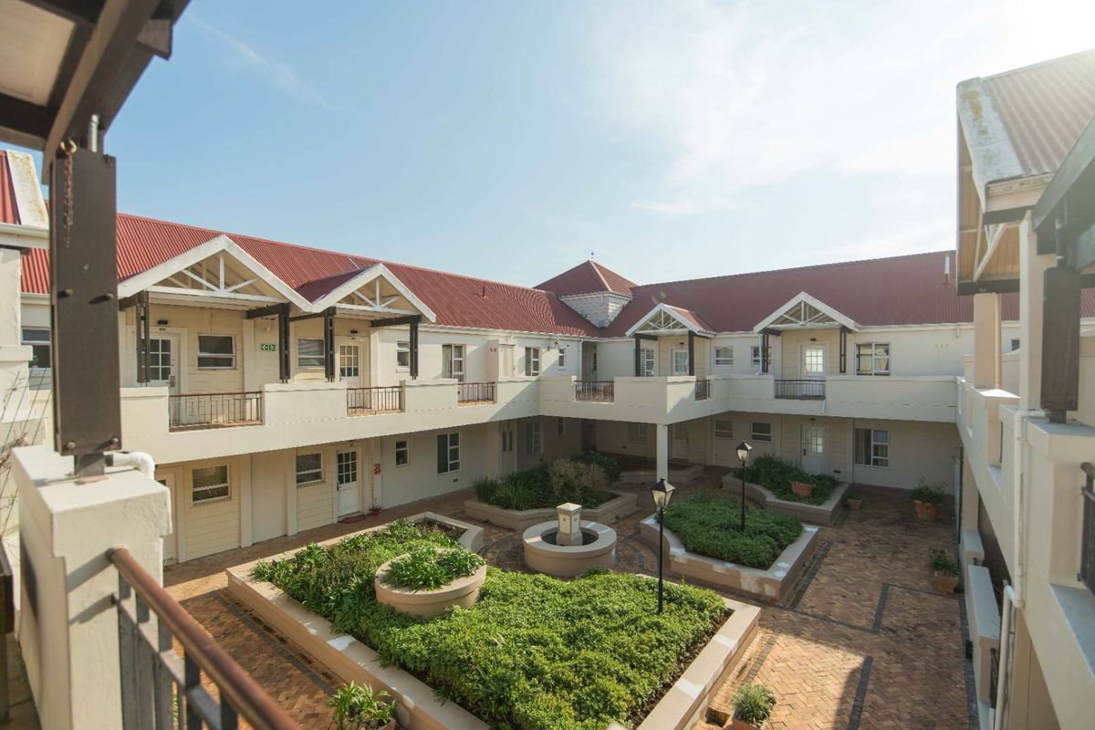 A well-maintained apartment complex courtyard featuring brick paving, raised garden beds, and a central water feature with surrounding balcony access.