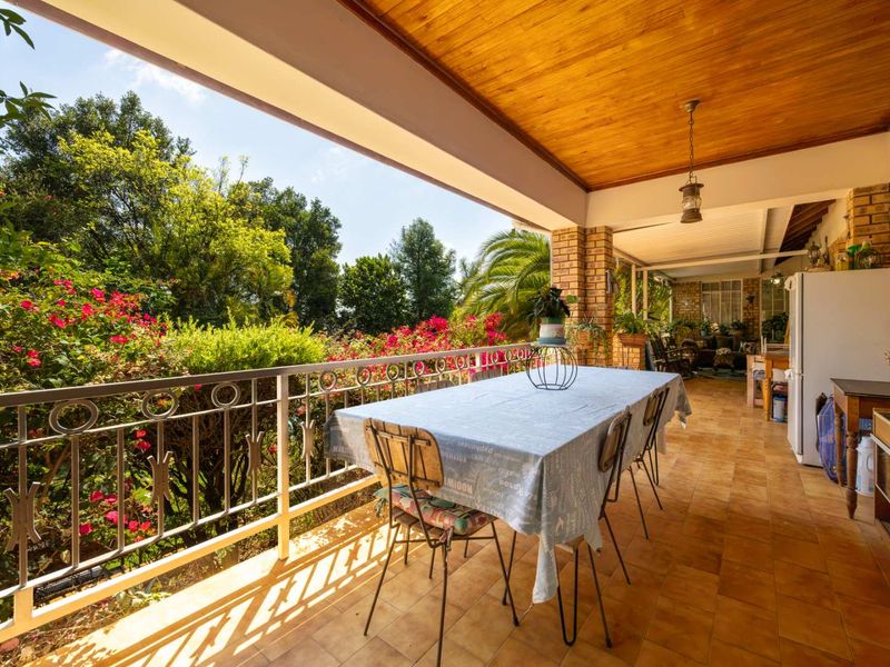 Spacious covered patio featuring a timber ceiling, brick pillars, and tiled flooring, overlooking a lush garden with vibrant flowering shrubs.