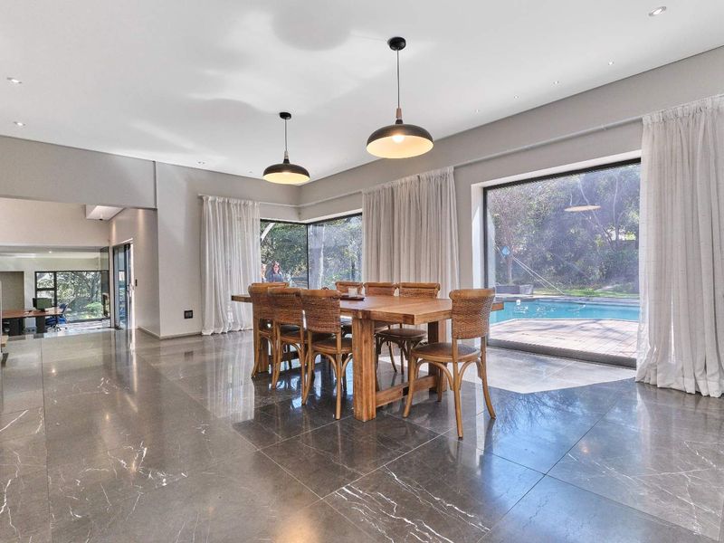 Spacious dining area featuring large format polished floor tiles, modern pendant lighting, and expansive sliding glass doors providing direct access to the pool area.
