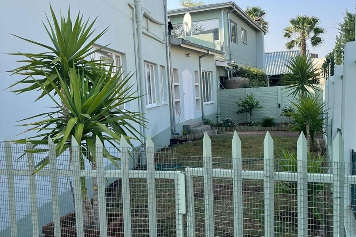 Rear view of the townhouse featuring a private garden area, metal security fencing, and painted masonry exterior walls.