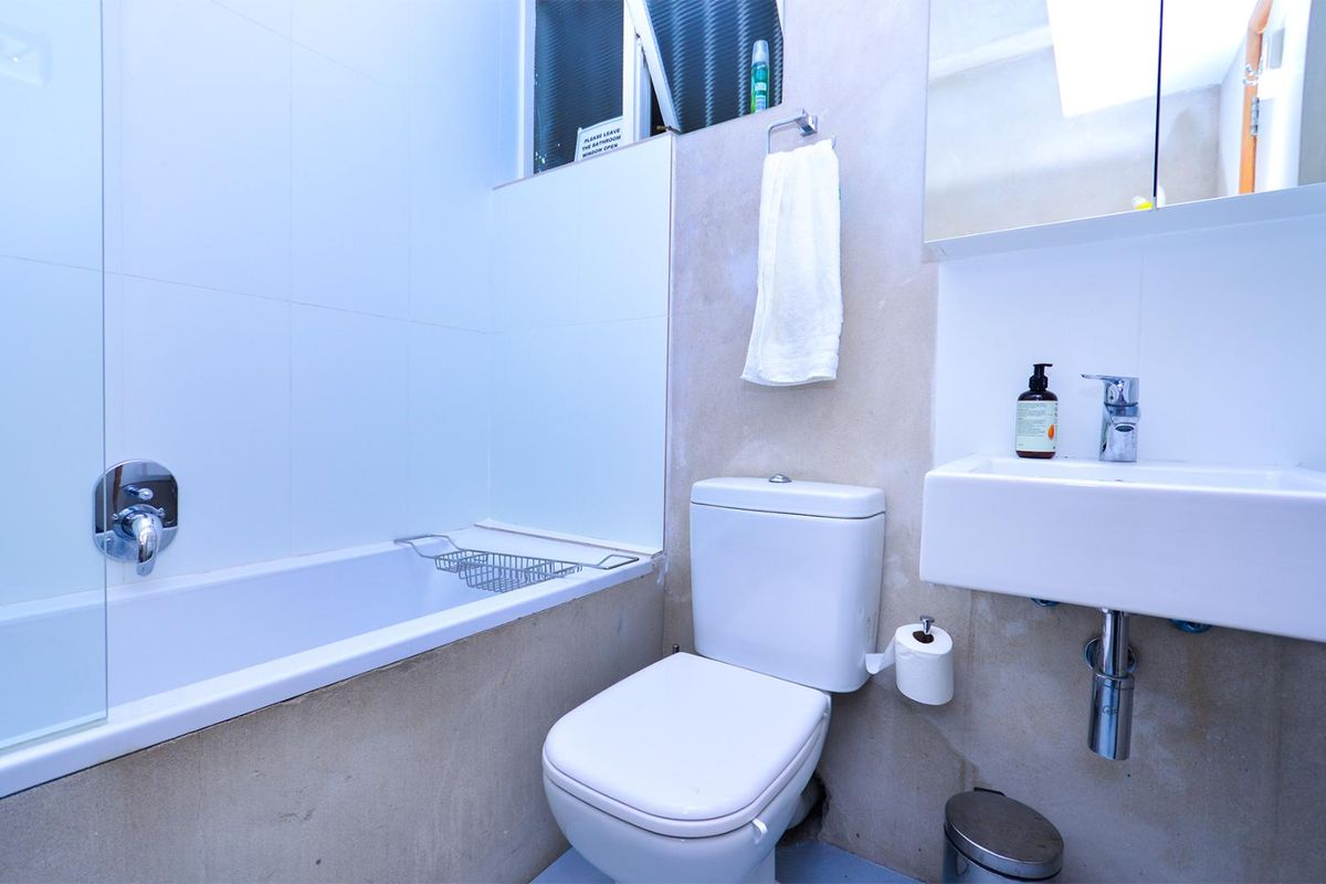 Compact bathroom featuring a bathtub, wall-mounted basin, and toilet, with unfinished wall surfaces requiring cosmetic attention.