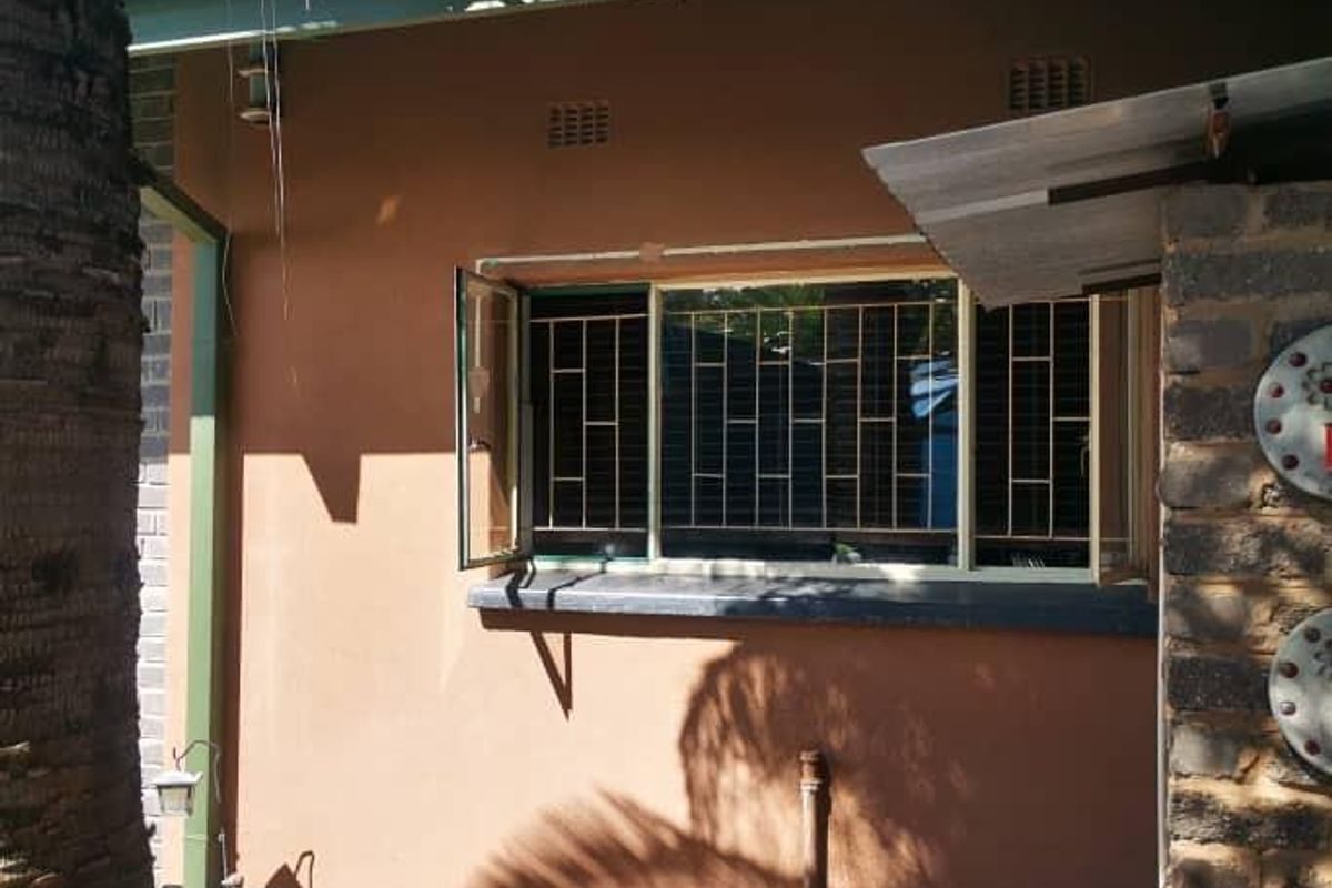 A view of the rear exterior wall featuring a window with security bars, a small paved area, and established garden surroundings.