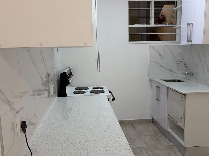 A compact, modern kitchen featuring marble-look splashbacks, quartz countertops, a stainless steel sink, and a freestanding electric stove.