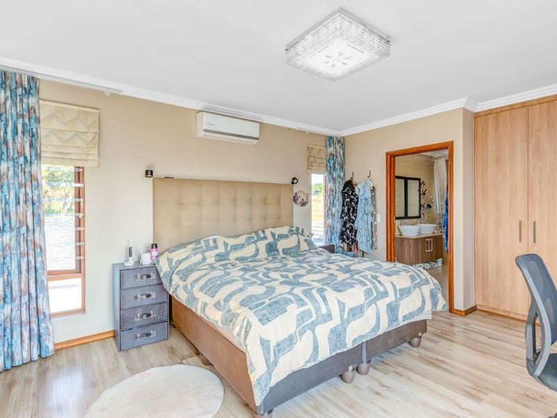 Spacious bedroom featuring laminate flooring, built-in cupboards, an air conditioning unit, and direct access to an en-suite bathroom.