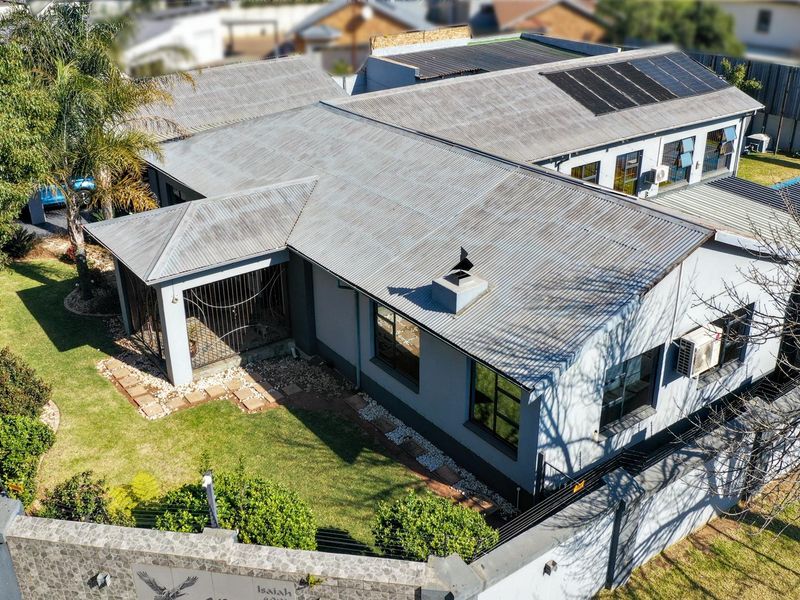 Aerial view of the property featuring a corrugated metal roof with solar panels, a landscaped garden, and secure perimeter walling.